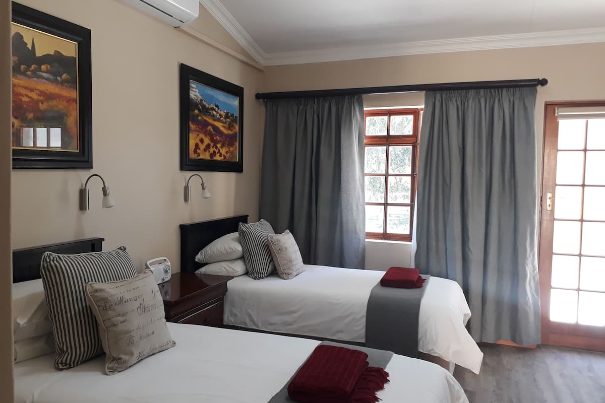 Habitación de hotel con dos camas, una ventana con cortinas, un equipo de aire acondicionado y lámparas fijadas a la pared.