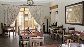 A dining area with wooden furniture, a chandelier, and a large window with curtains. - 17 on Bird Guest House (Beaufort West)