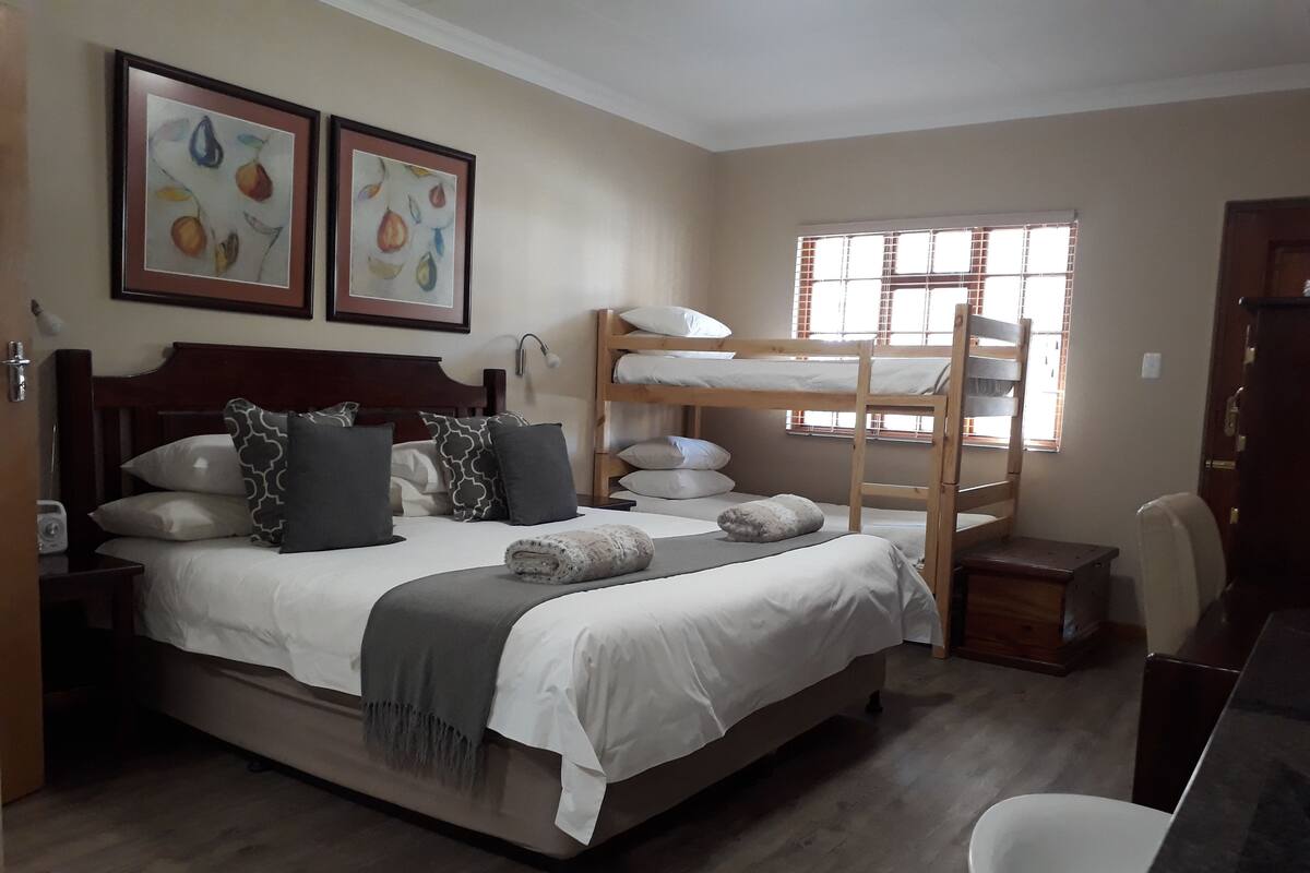Un dormitorio con una cama individual, una litera, una mesita de noche, una silla y una ventana con persianas.