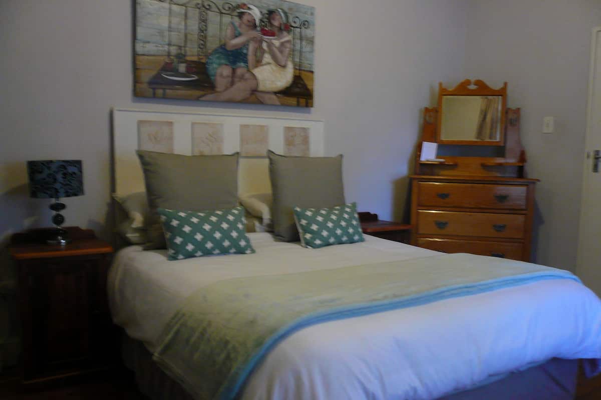 Un dormitorio con cama, cómoda, mesita de noche, lámpara y un cuadro en la pared.