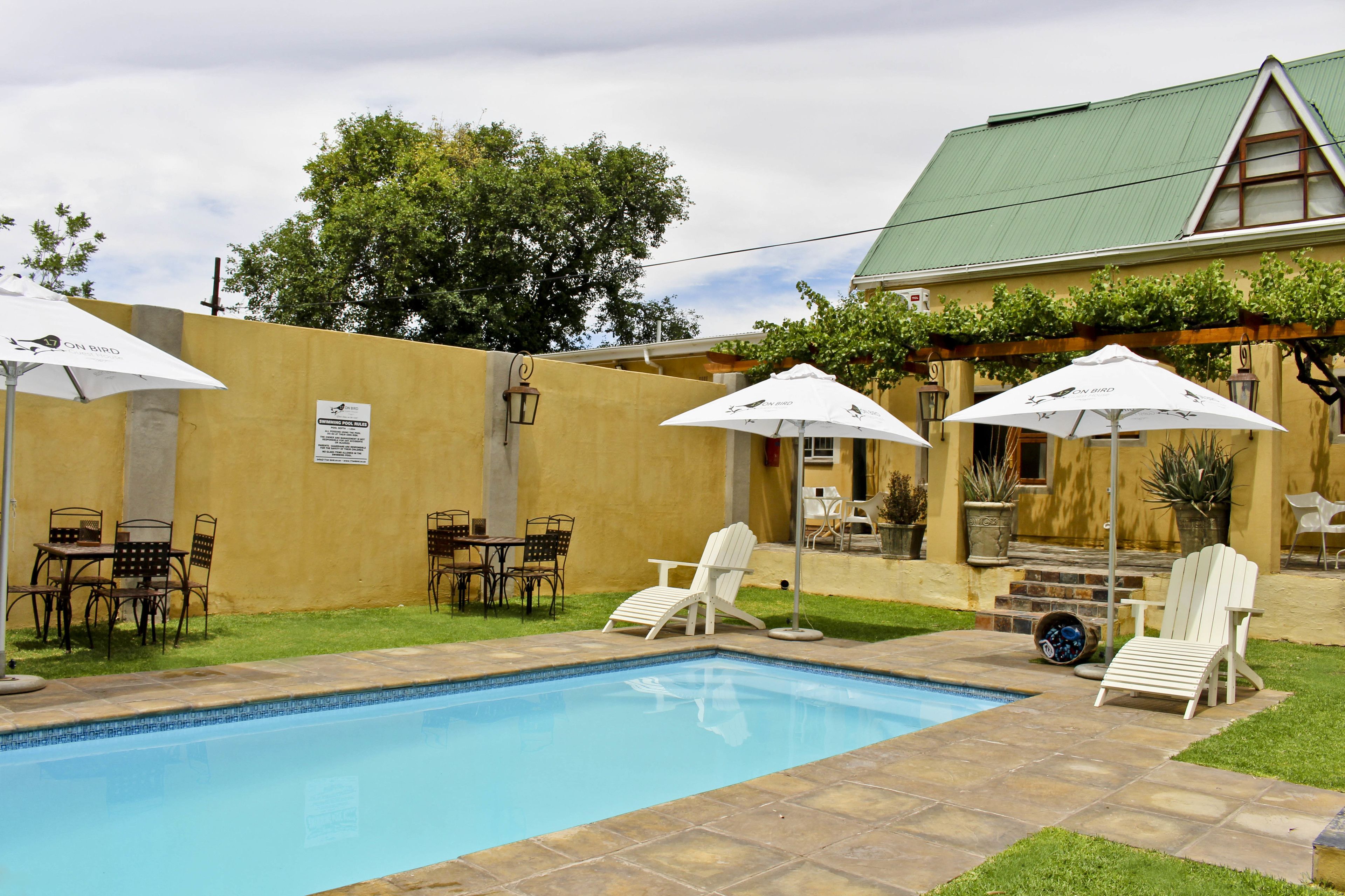 Ein Swimmingpool mit Liegestühlen und Sonnenschirmen, umgeben von einer Terrasse mit Tischen und Stühlen.