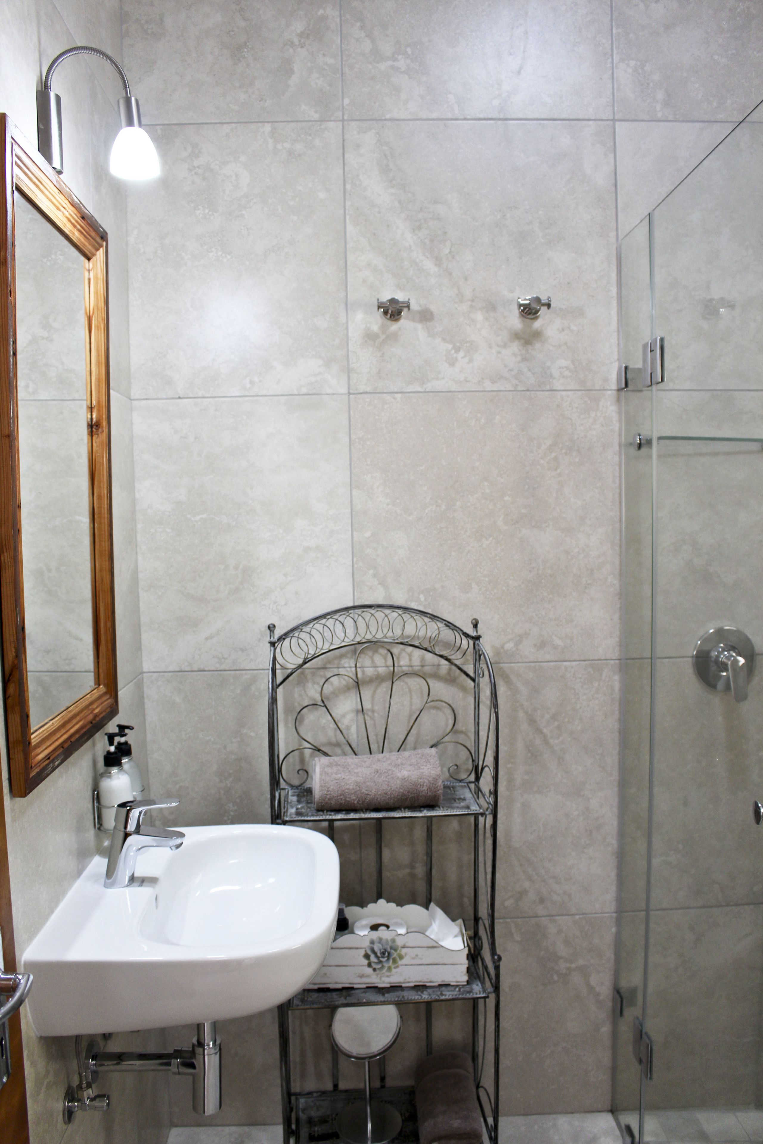 Une salle de bain avec un lavabo blanc, un porte-serviettes en métal, un miroir et une cabine de douche en verre.