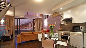 A modern living room with a sofa, dining table, chairs, and a kitchen area with a microwave and oven. - Adderley Apartments (Cape Town)