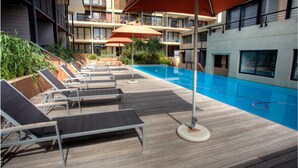 A poolside area with lounge chairs and umbrellas, surrounded by a wooden deck and a building with balconies. - Adderley Apartments (Cape Town)