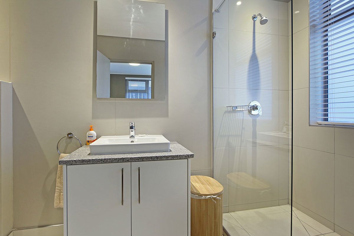 A modern bathroom with a glass shower enclosure, a sink with a mirror above it, and a toilet with a wooden seat.