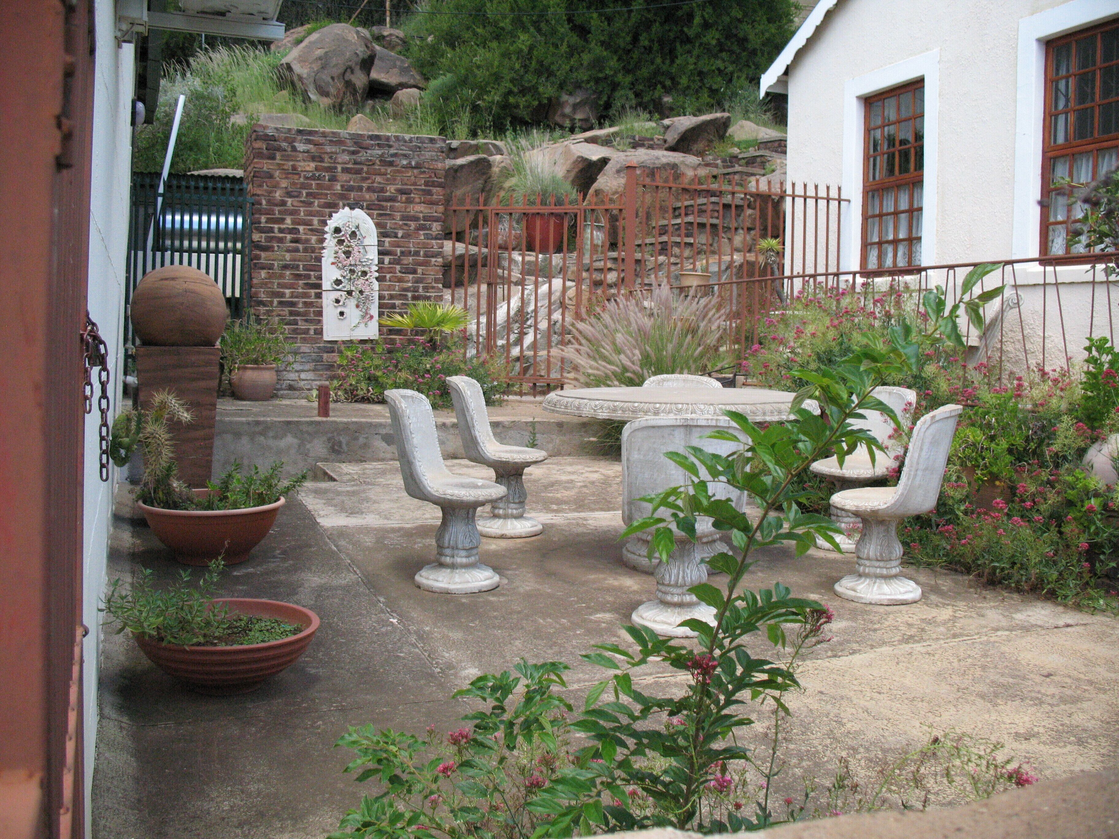 A courtyard with stone chairs, a brick wall, and potted plants.