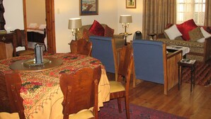 A cozy living room with a dining table, chairs, a sofa, and a coffee table. There are two lamps on the sofa and a painting on the wall.