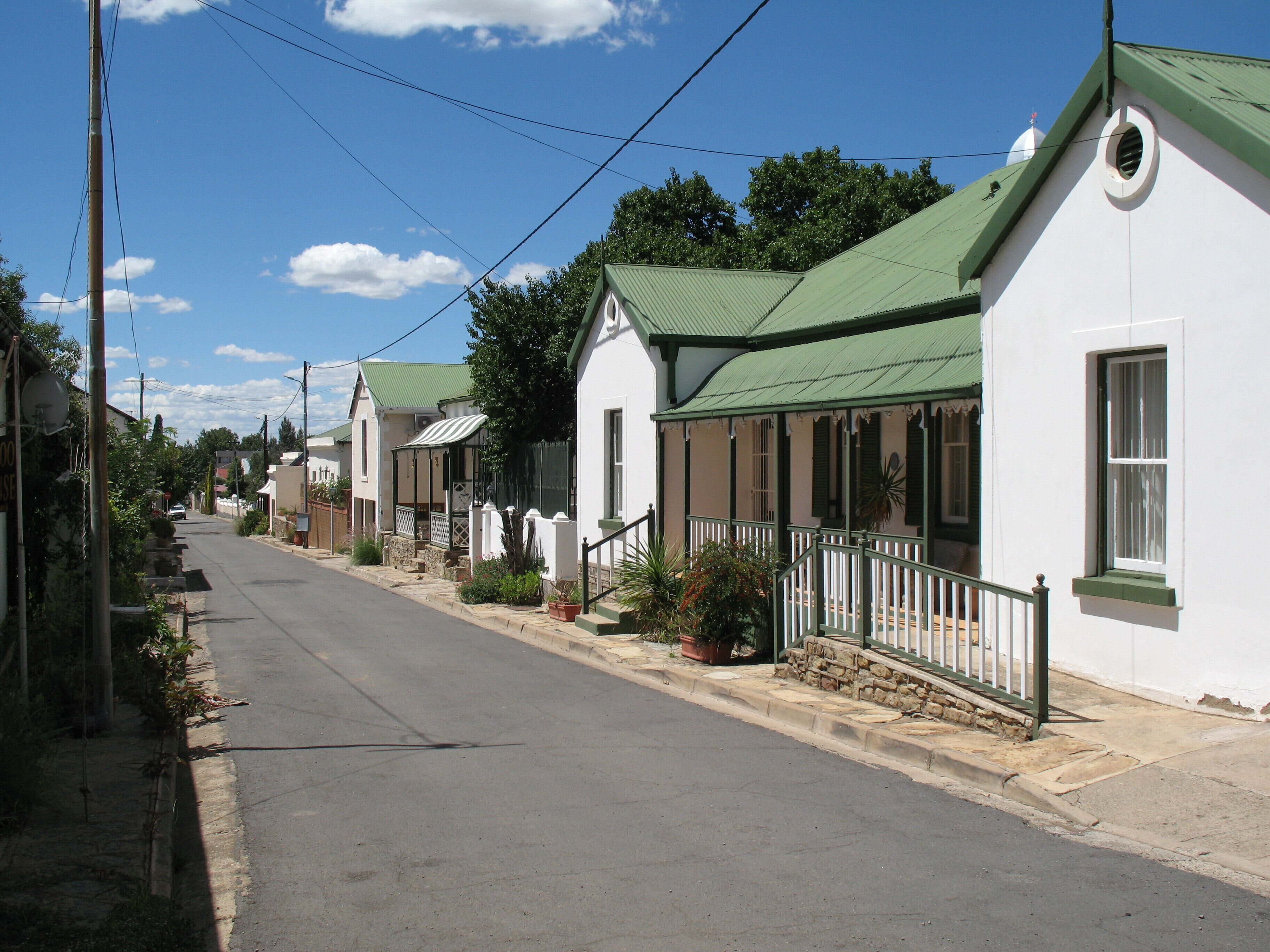 A row of white houses with green roofs and white walls, a clear sky, and a quiet street.