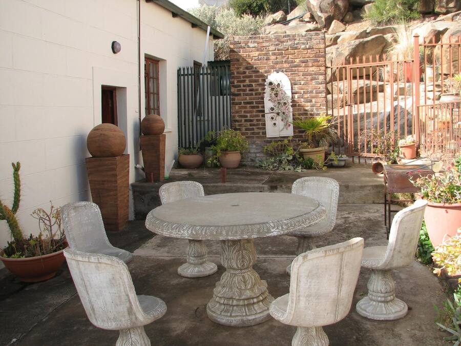 A patio with a round table and four chairs, surrounded by potted plants and a brick wall.