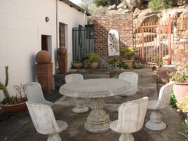 Un patio con una mesa redonda y cuatro sillas, rodeado de macetas con plantas y un muro de ladrillo.