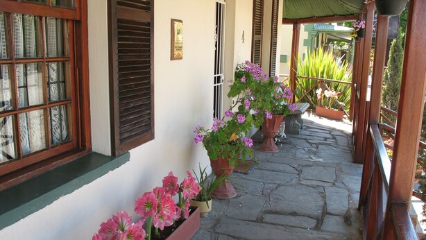 A stone-paved porch with potted pink flowers and a wooden railing.