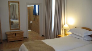 A hotel room with a bed, a bedside table with a lamp, a wooden dresser, and a mirror.