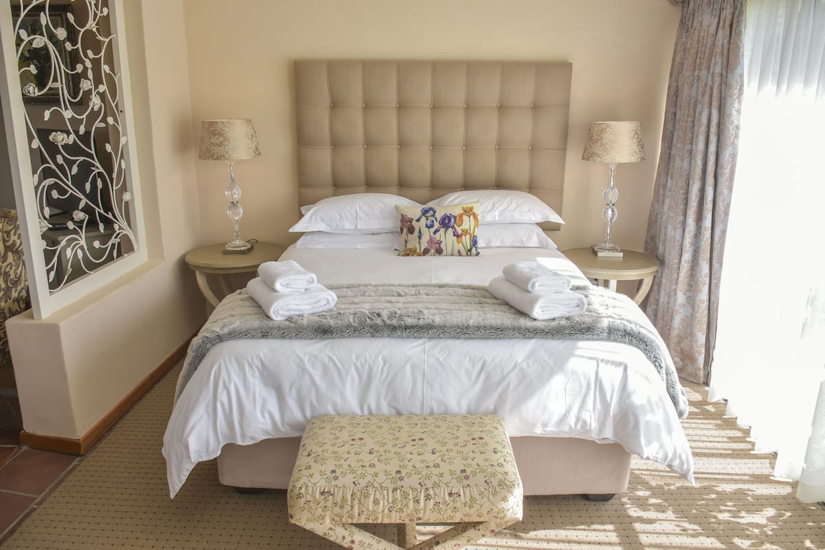 A neatly made bed with white linens, a fluffy beige headboard, and two bedside lamps.