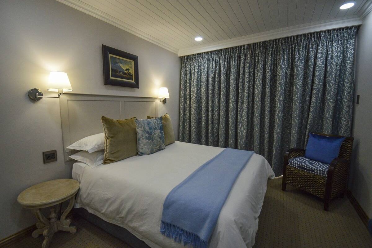 A hotel room with a bed, two bedside lamps, a chair, and a window with patterned curtains.