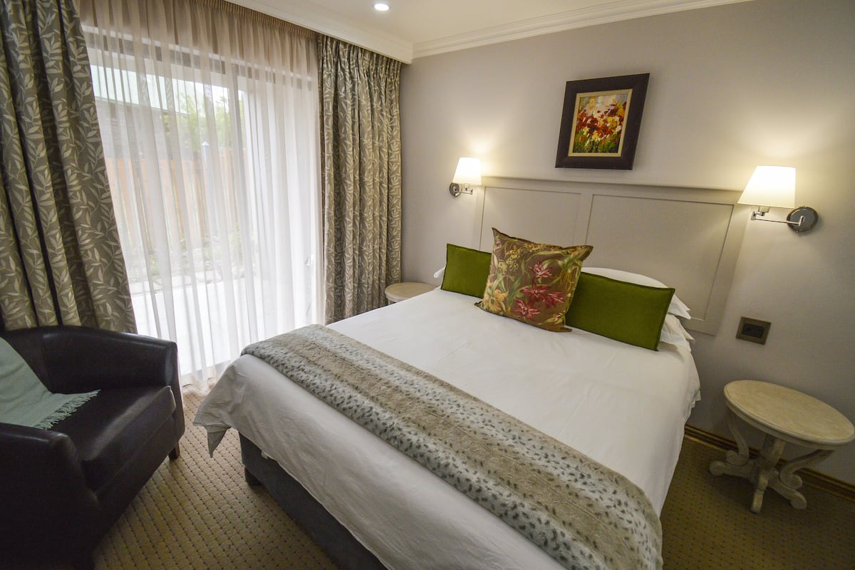 A hotel room with a bed, a chair, a small table, and a painting on the wall.