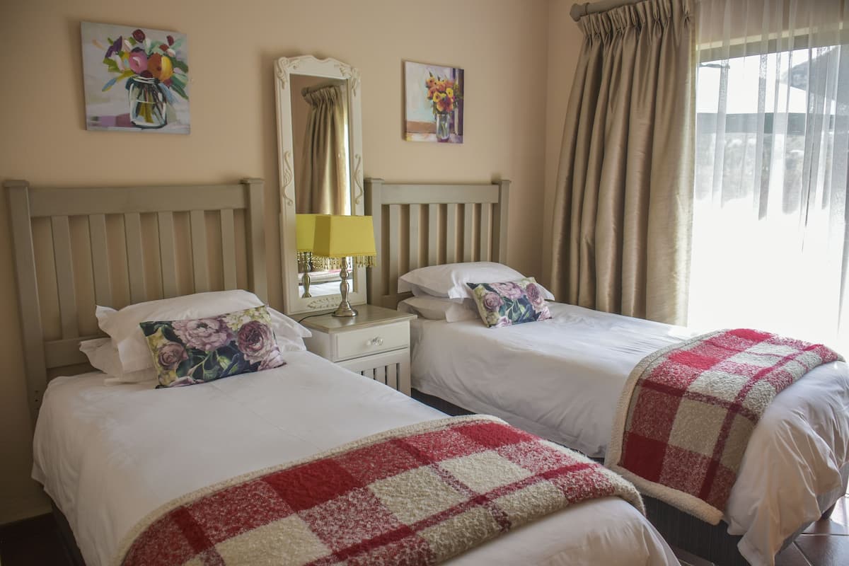 A hotel room with two beds, a nightstand with a lamp, and artwork on the walls.