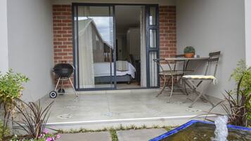 A balcony with a sliding glass door leading to a bedroom, a small table with a potted plant, and a water feature.