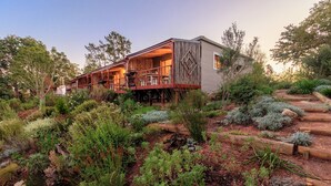Un chalet rustique doté d’une terrasse en bois et d’un jardin où poussent différentes espèces de plantes.