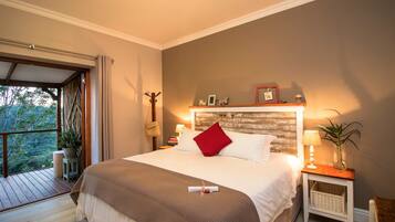 A bedroom with a large bed, a wooden headboard, a nightstand with a lamp, and a view of the outdoors.