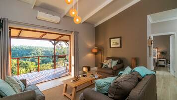 Ein gemütliches Wohnzimmer mit einem großen Schiebeglastür, die auf einen Balkon führt, einem Holztisch und zwei Sofas mit Kissen.