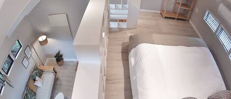 Un dormitorio moderno con una cama grande, un pequeño rincón de descanso y una escalera que lleva a un nivel superior.