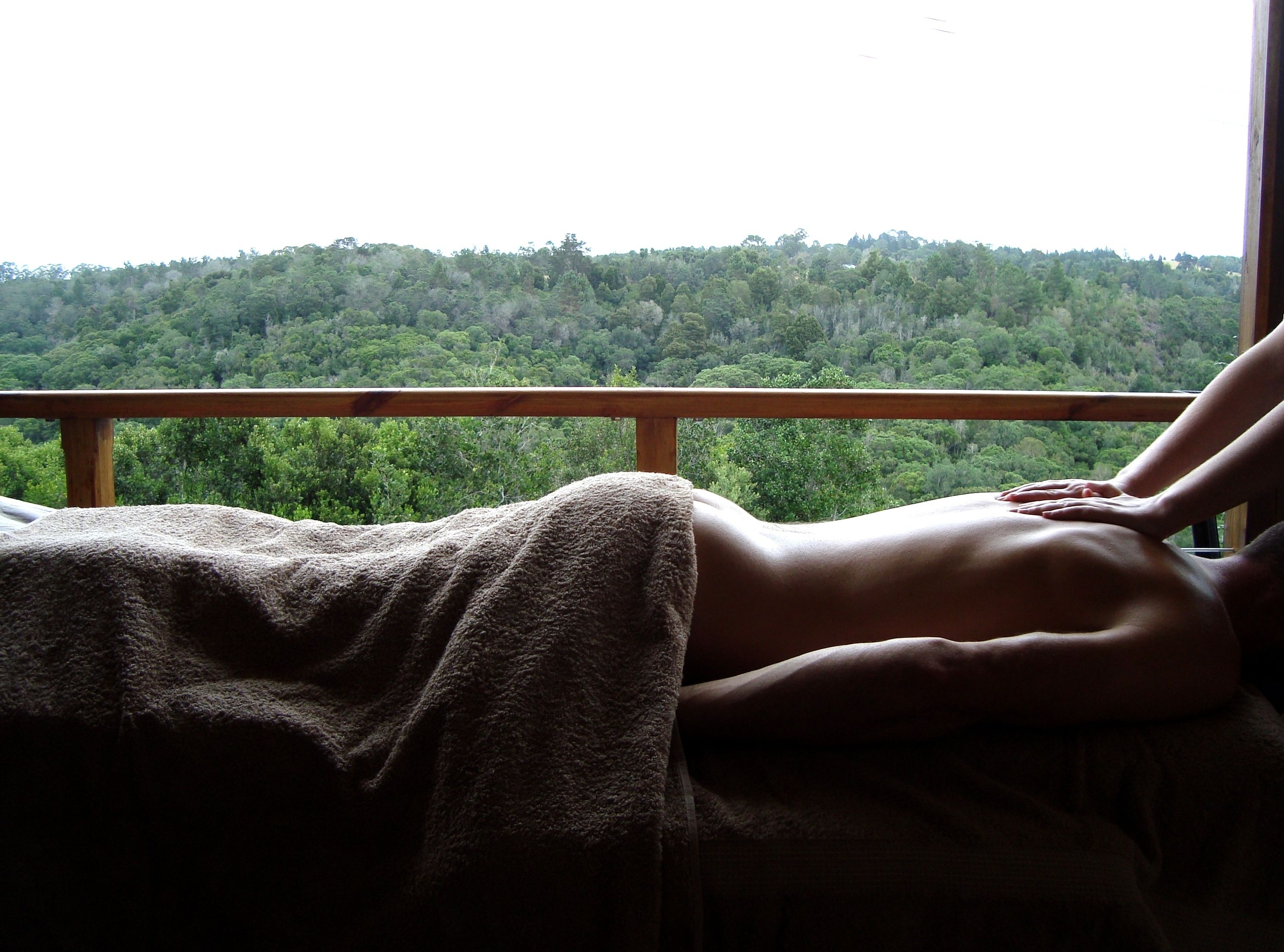A person lying on a bed with a view of a forested landscape through a window.