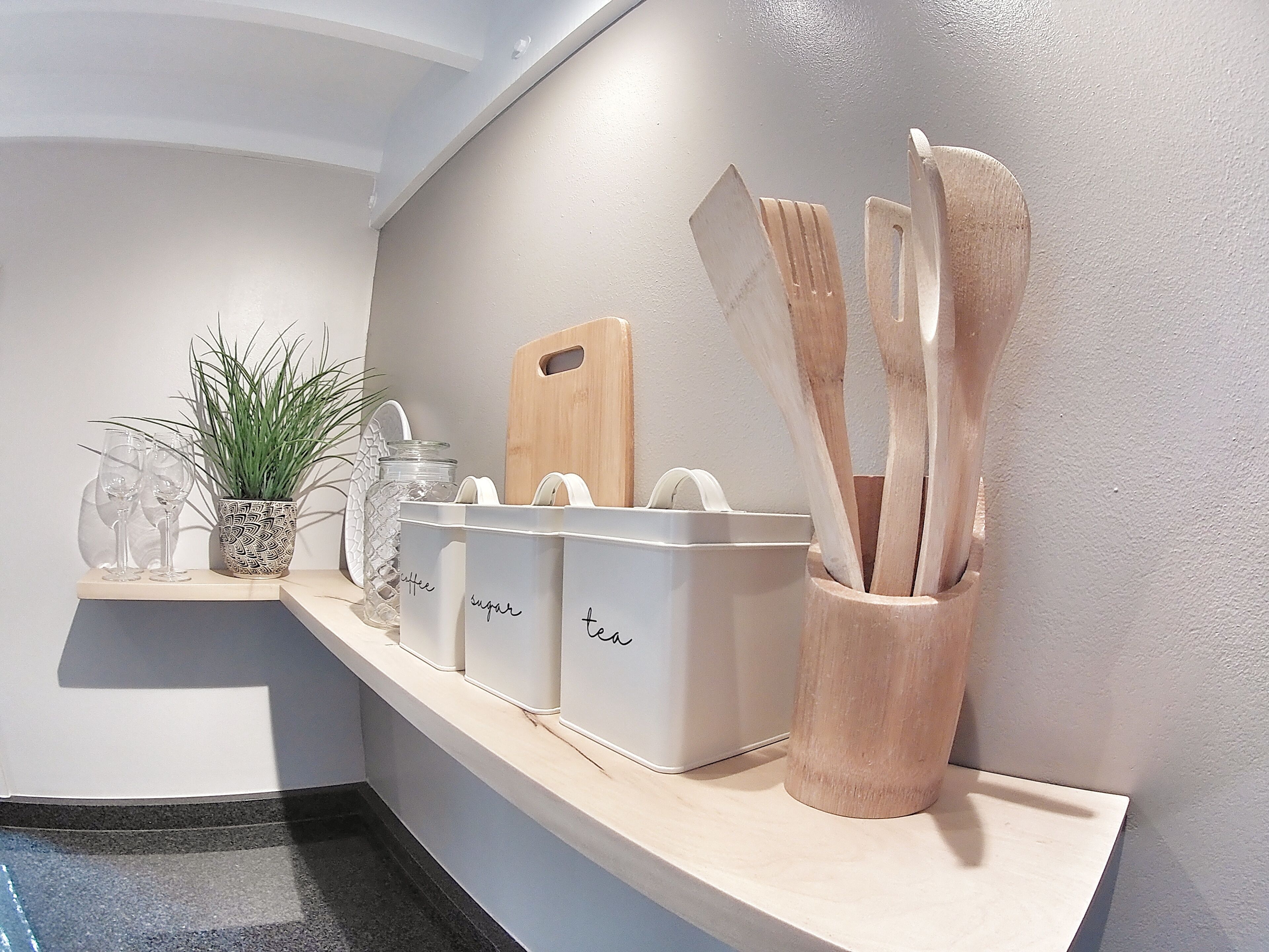 Una encimera de cocina con recipientes de almacenamiento etiquetados para café, azúcar y té, una tabla de cortar y utensilios de madera.