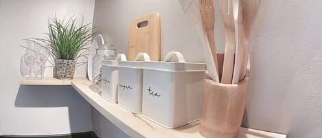 Una encimera de cocina con recipientes de almacenamiento etiquetados para café, azúcar y té, una tabla de cortar y utensilios de madera.