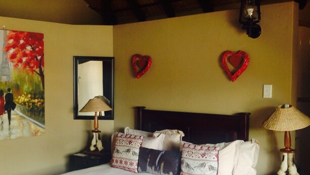 Un dormitorio con una cama, dos mesitas de noche, una lámpara, un espejo y dos adornos con forma de corazón en la pared.