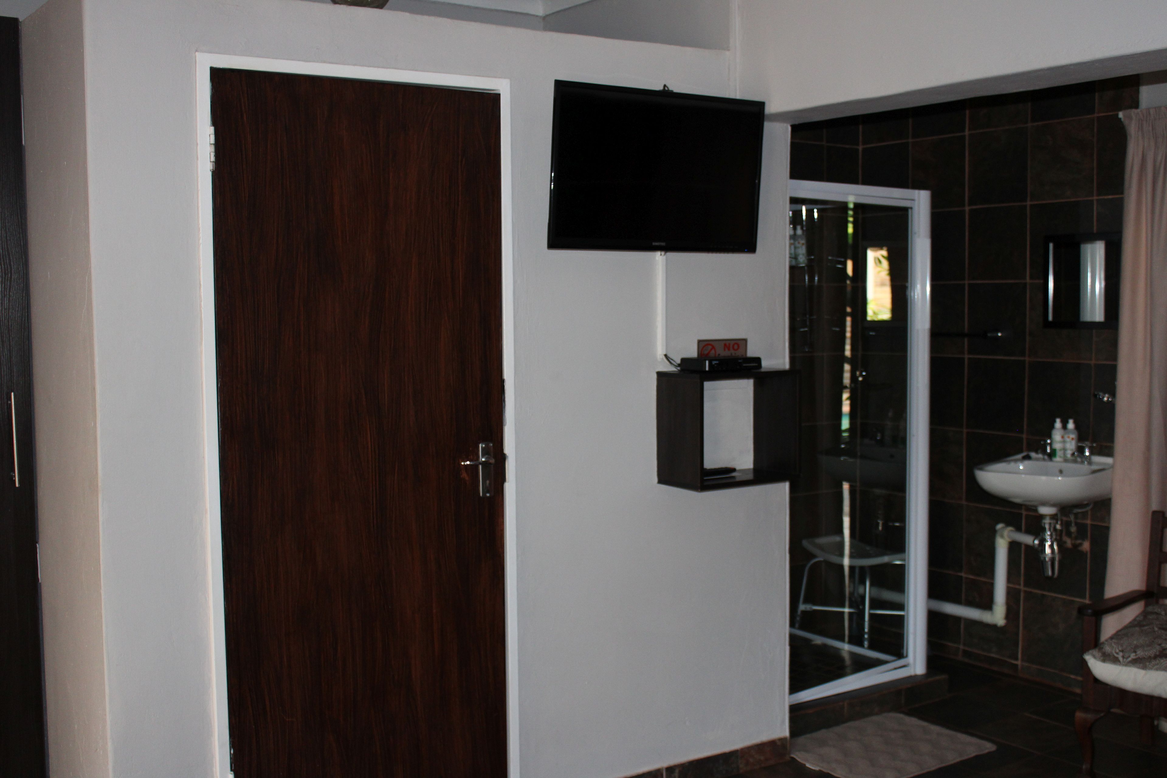 Un baño con puerta de madera, televisor montado, cabina de ducha de vidrio y lavamanos.