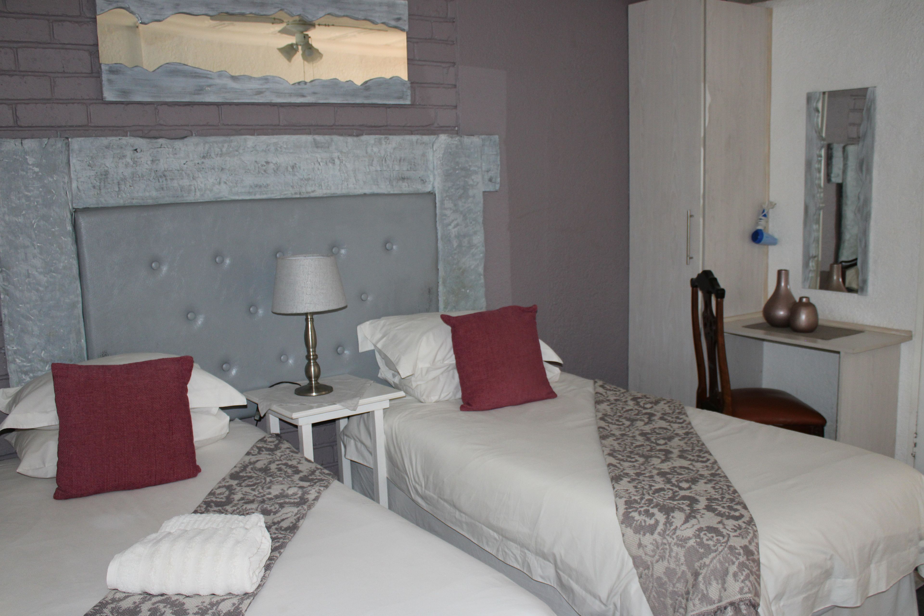 Quarto de hotel com duas camas, mesa de cabeceira, luminária, espelho e uma pequena mesa.