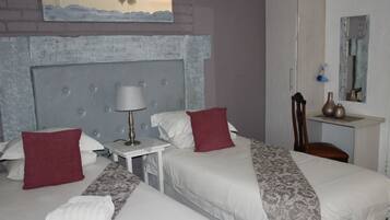 Quarto de hotel com duas camas, mesa de cabeceira, luminária, espelho e uma pequena mesa.