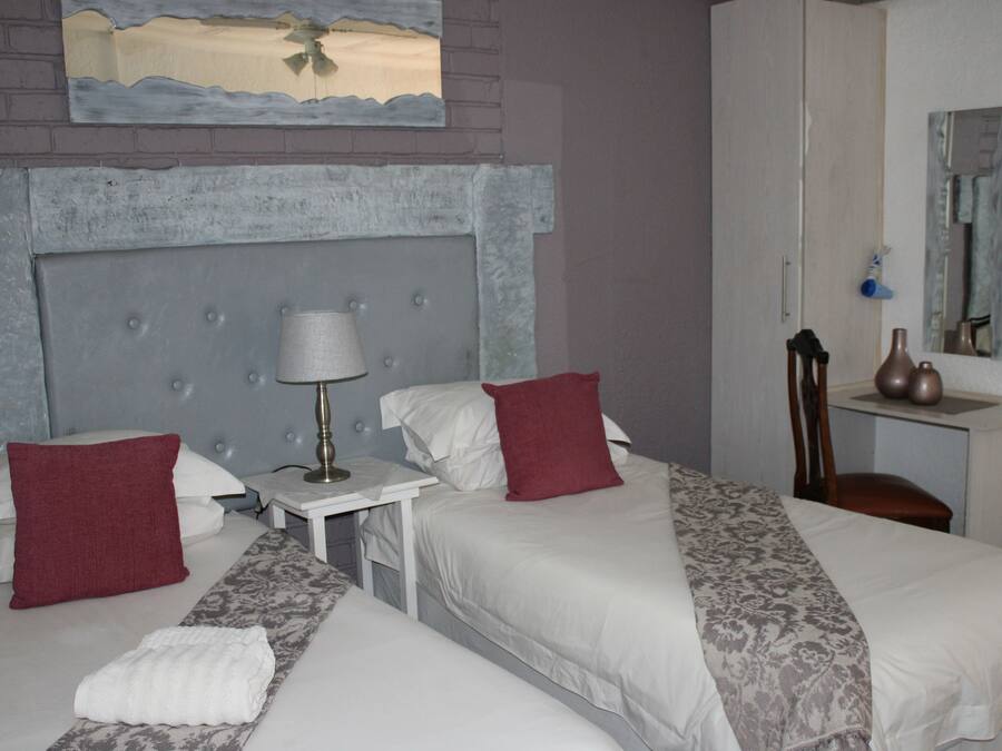 Quarto de hotel com duas camas, mesa de cabeceira, luminária, espelho e uma pequena mesa.
