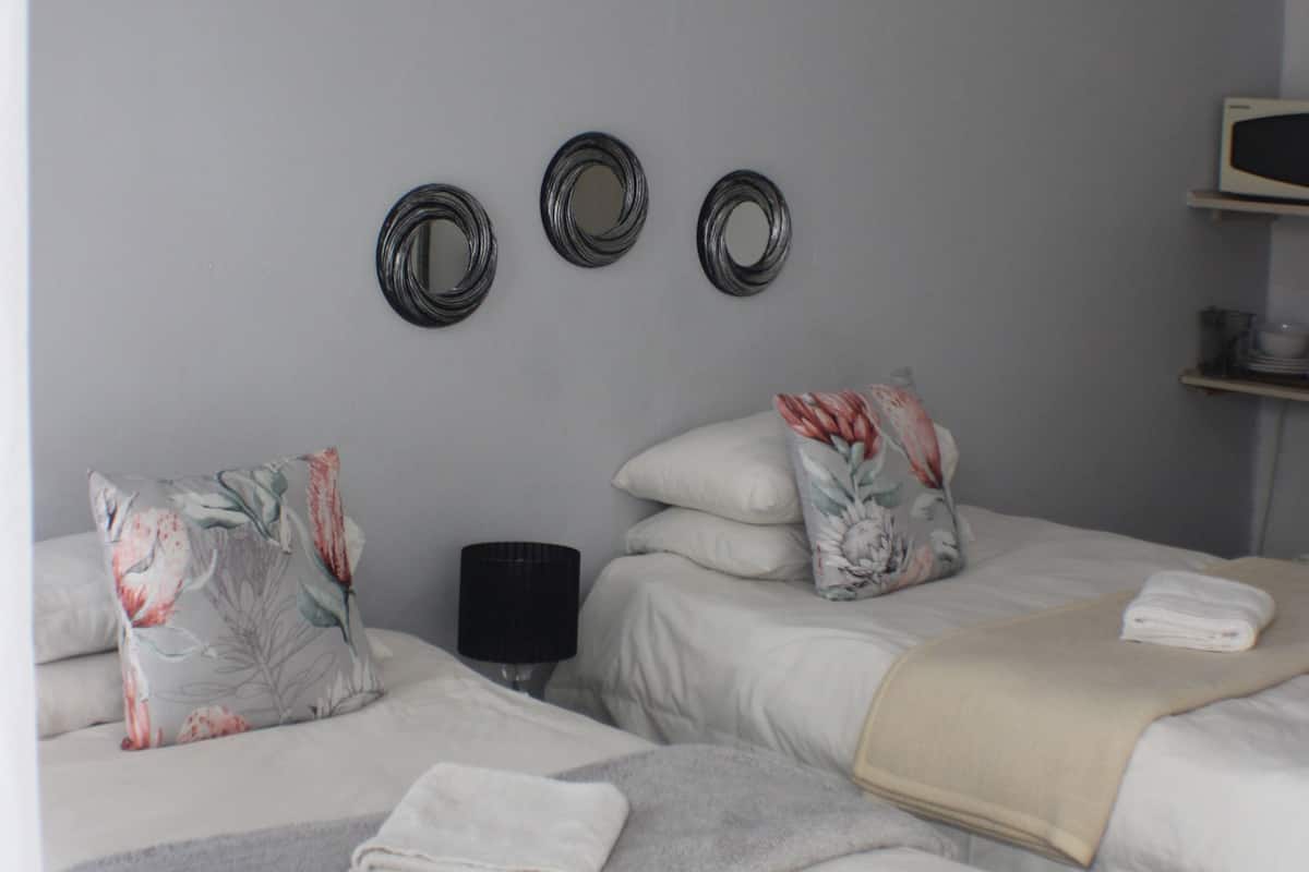 A bedroom with two beds, a bedside table, and wall-mounted mirrors.