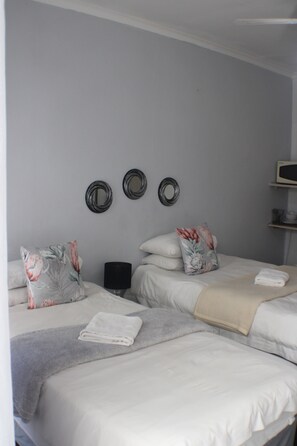 A bedroom with two beds, a bedside table, and wall-mounted mirrors. - Ukarimu Guest House (Klerksdorp)