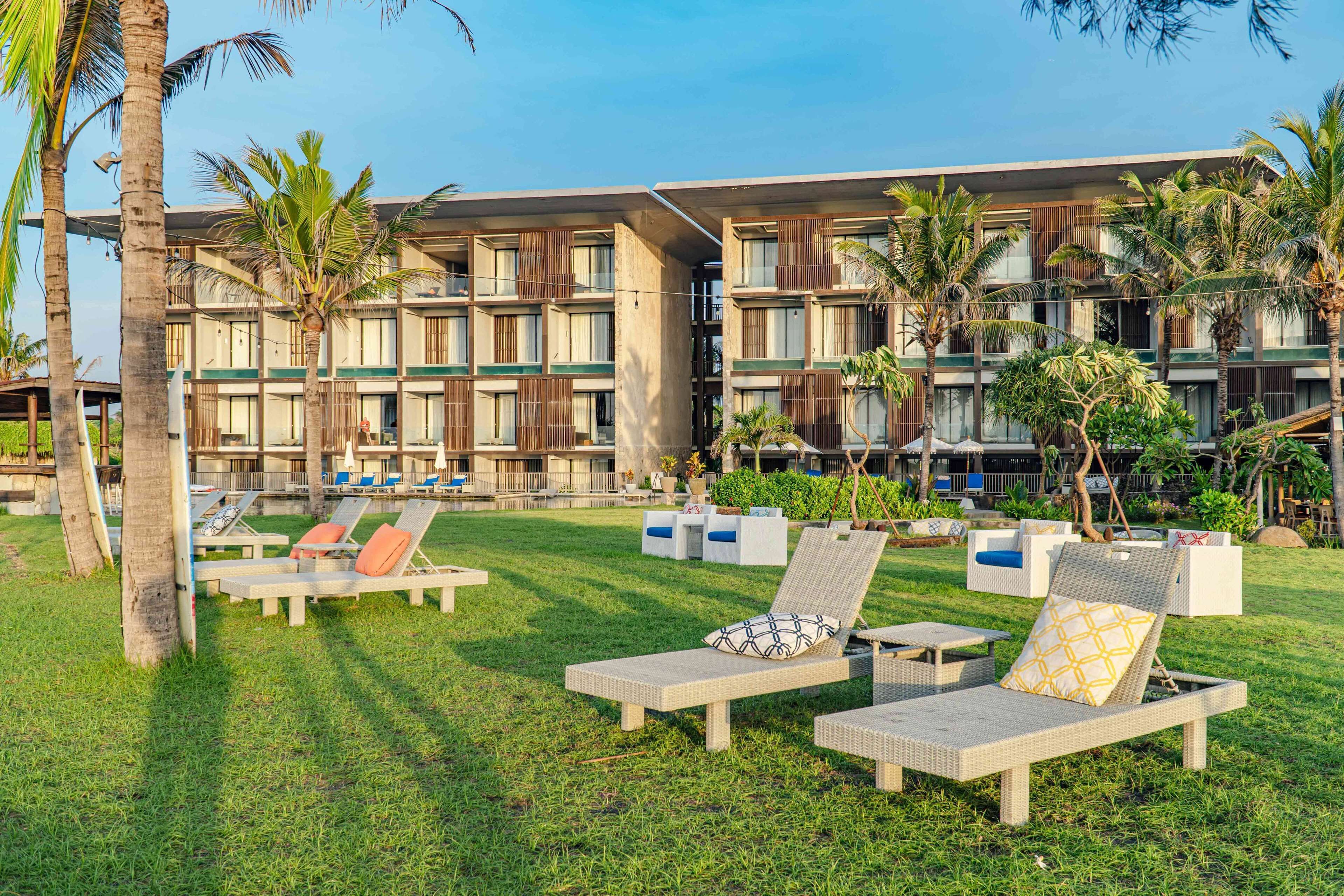 A hotel with outdoor lounge chairs, palm trees, and a modern building facade.