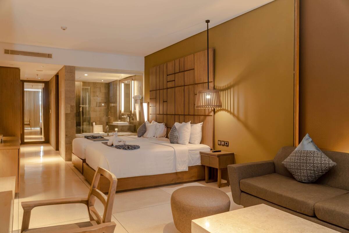 Une chambre d’hôtel moderne dotée d’un grand lit, d’un coin salon avec un canapé et un pouf, d’un bureau et d’un miroir.