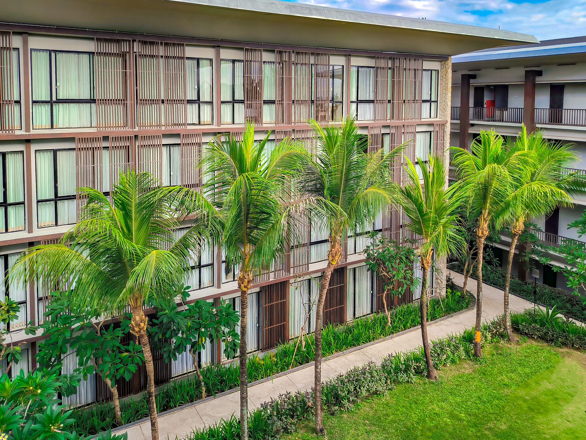 Un hotel de varios pisos con un diseño moderno, que cuenta con un patio central con palmeras y un camino.