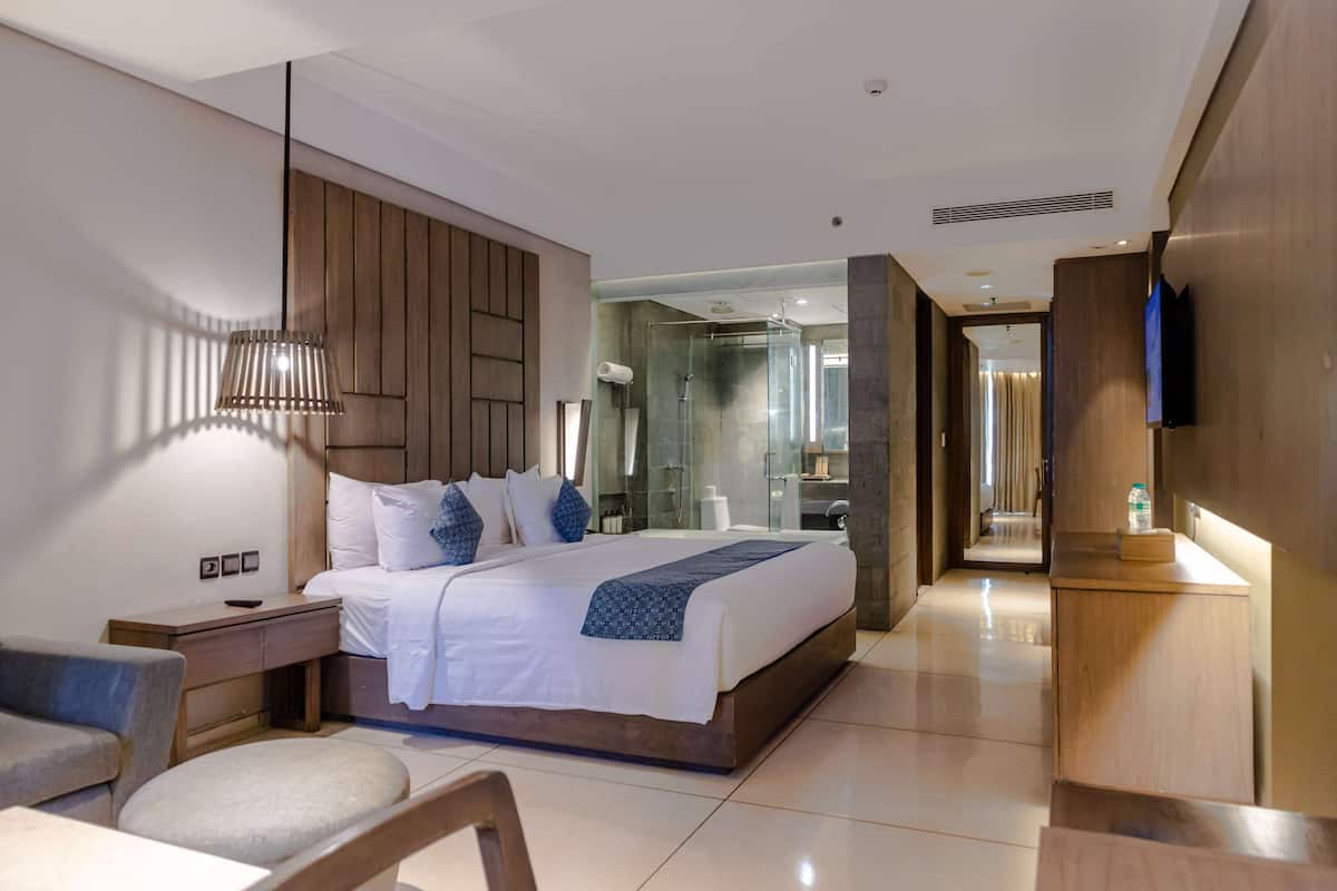Une chambre d’hôtel moderne, dotée d’un grand lit, de tables de chevet, d’une télévision et d’une salle de bain avec une douche en verre.
