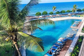 A resort pool with clear blue water, surrounded by palm trees and lounge chairs. - Wyndham Tamansari Jivva Resort Bali (Banjarangkan)