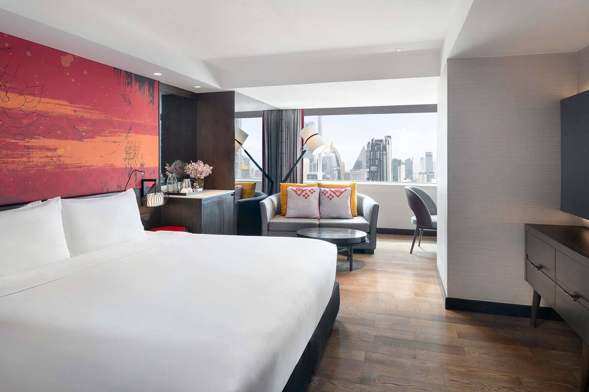 Una habitación de hotel moderna con una cama grande, un escritorio, un sofá y vistas a la silueta urbana.