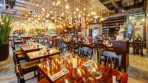 Een restaurant met meerdere tafels, hangende lampen en bakstenen muren.