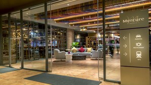 Een moderne hotel lobby met glazen entree, een zithoek en bewegwijzering naar parkeerplaats, restaurant en BTS.