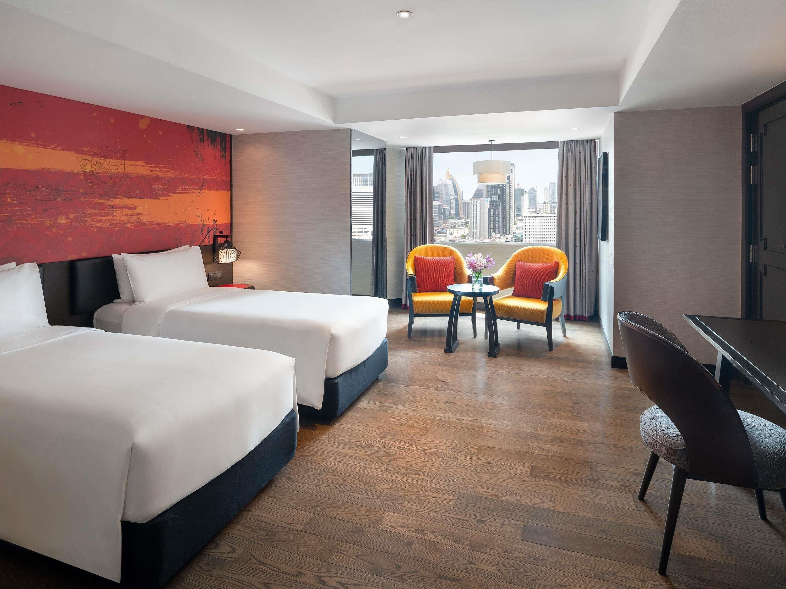 A hotel room with two beds, a seating area with chairs, a small table, and a city view.