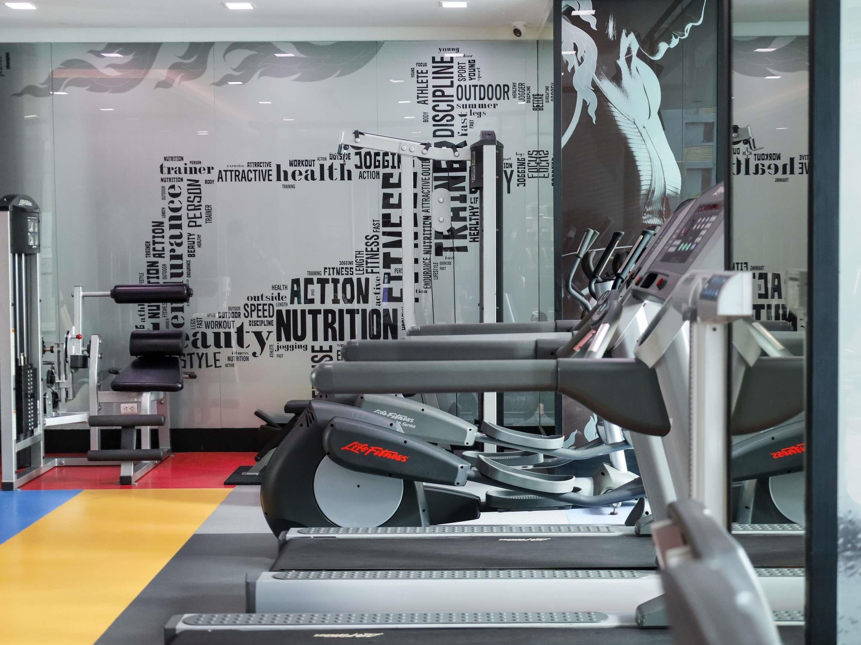 Ein Fitnessstudio mit Laufbändern, Kraftgeräten und einer Wand mit Begriffen rund um das Thema Fitness.