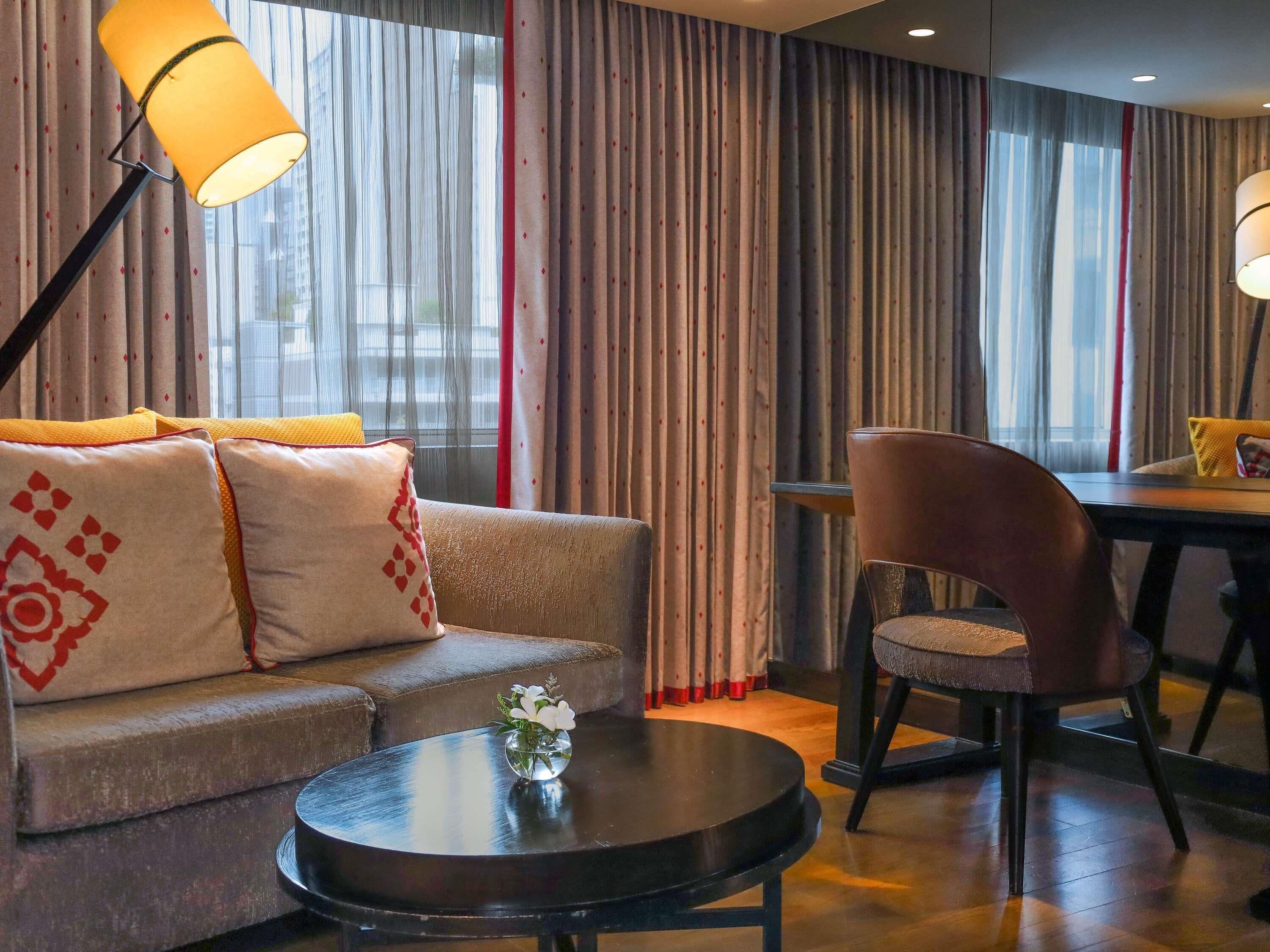 A hotel room with a sofa, a round table, a chair, and a lamp.