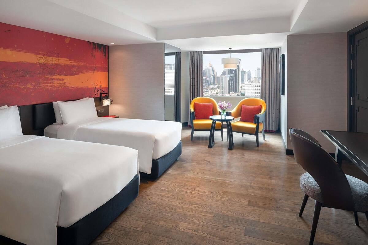Habitación de hotel con dos camas, una mesa de comedor y vistas a la ciudad.