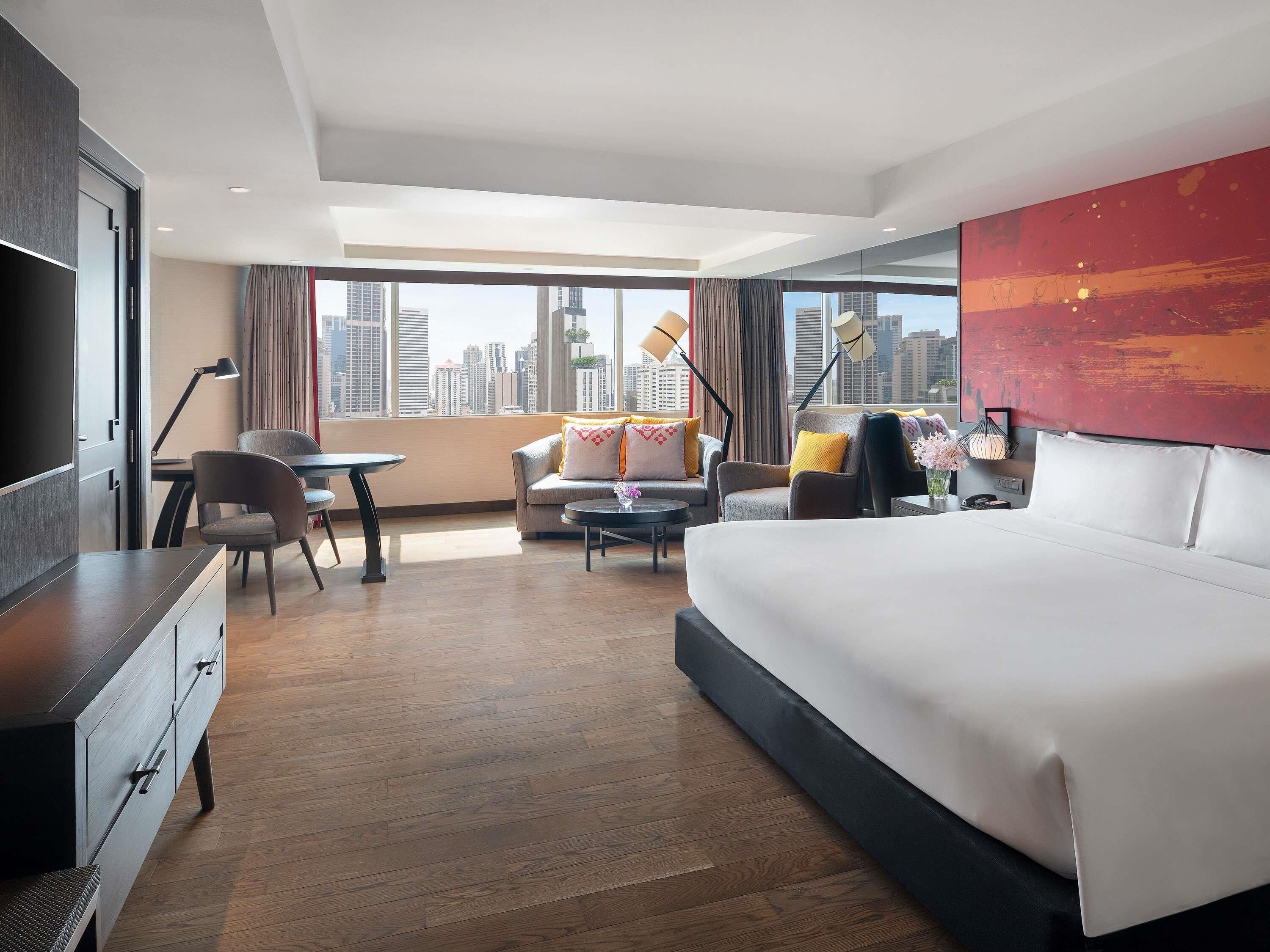 A hotel room with a bed, a desk, a chair, a sofa, and a view of the city skyline.