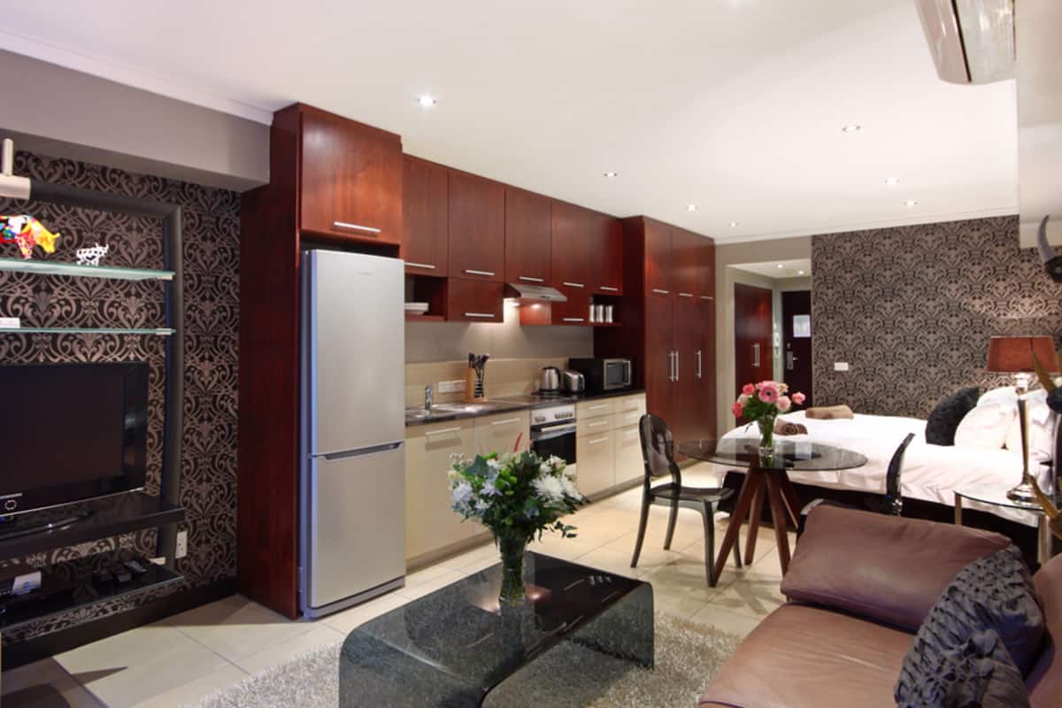 A modern hotel room with a kitchen, dining area, and a living space.