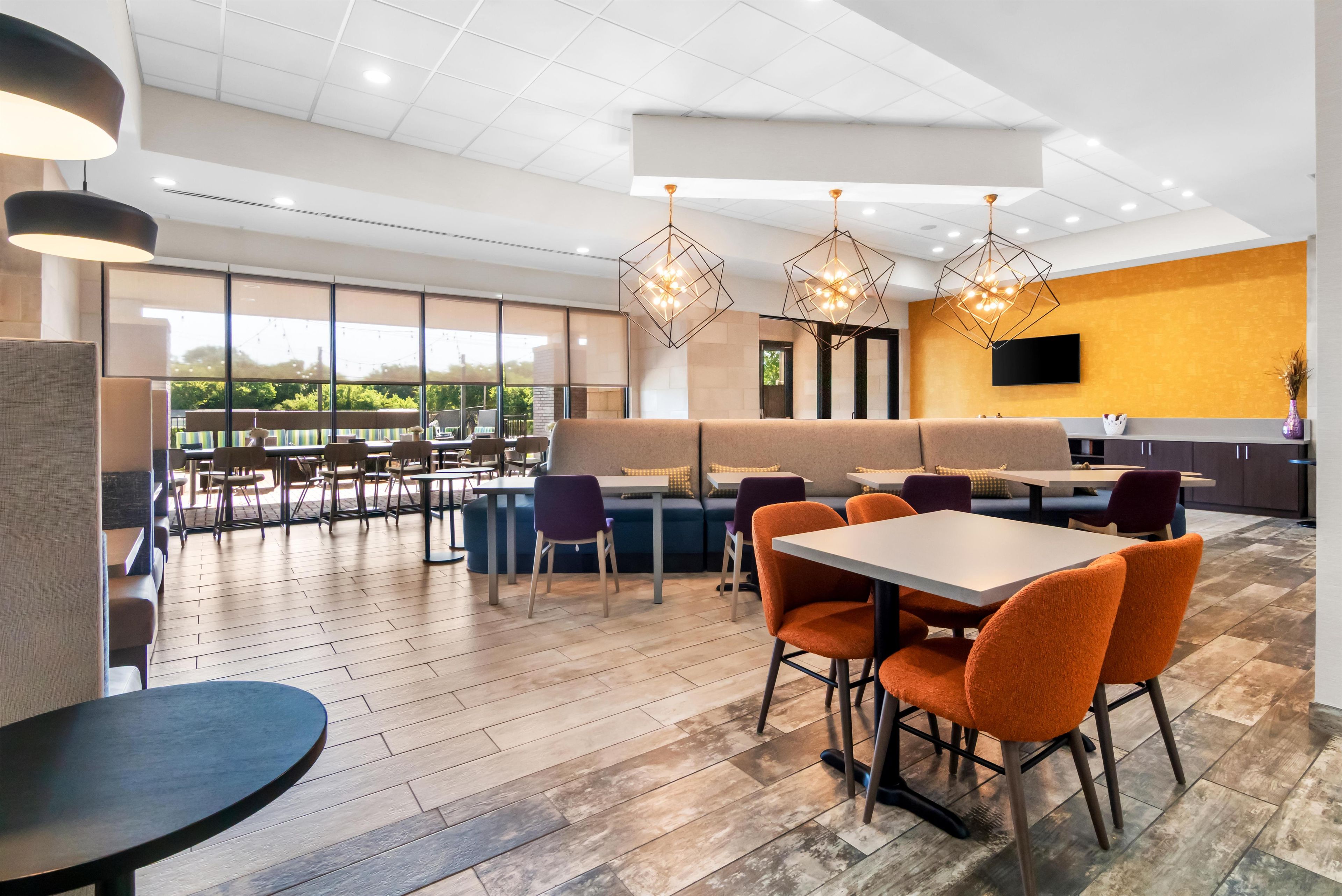 A modern dining area with a mix of seating options, including tables and booths, and a large window providing a view of the outdoors.